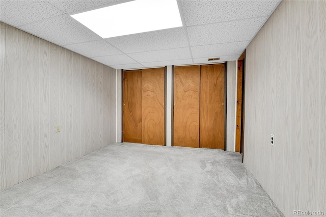 unfurnished bedroom with a paneled ceiling, carpet flooring, and two closets