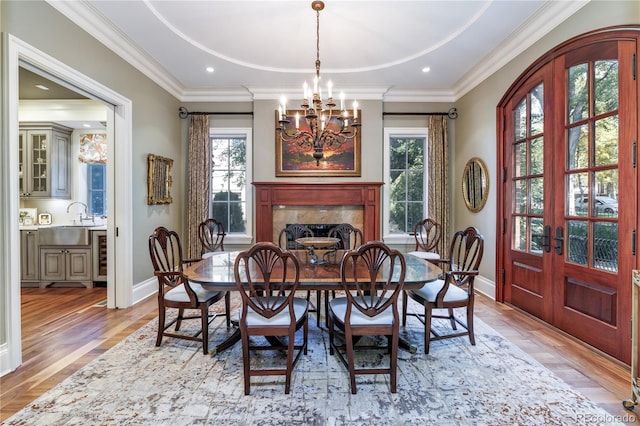 dining space featuring crown molding, an inviting chandelier, light hardwood / wood-style floors, a tiled fireplace, and french doors