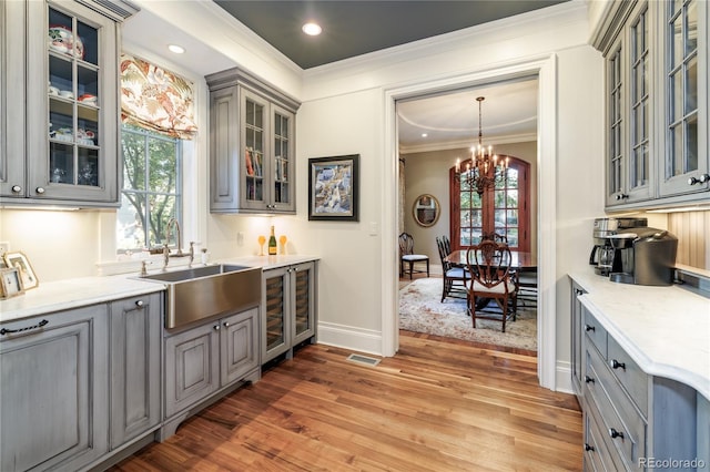 bar featuring sink, gray cabinets, light stone countertops, ornamental molding, and decorative light fixtures