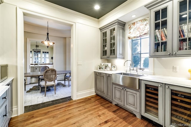 bar with sink, gray cabinets, hardwood / wood-style floors, decorative light fixtures, and beverage cooler