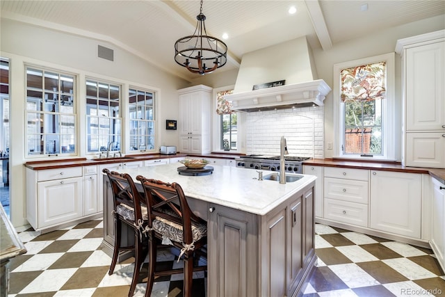 kitchen featuring a kitchen island with sink, pendant lighting, custom exhaust hood, and white cabinetry