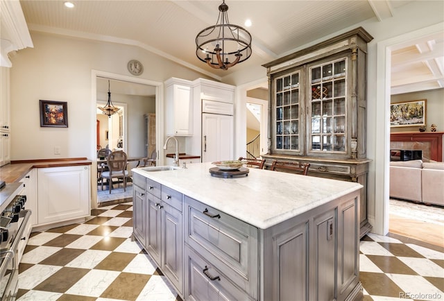 kitchen with gray cabinetry, hanging light fixtures, an island with sink, and white cabinets