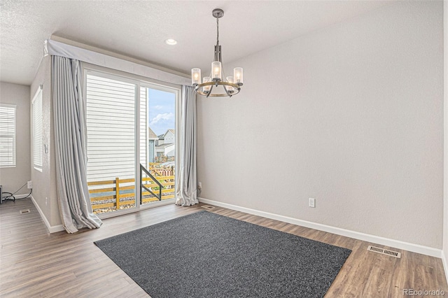 unfurnished dining area featuring an inviting chandelier, baseboards, wood finished floors, and visible vents