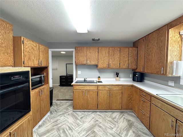 kitchen featuring black appliances, a textured ceiling, brown cabinetry, and light countertops