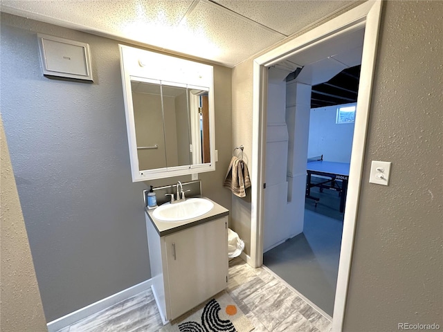 bathroom with a textured wall, a paneled ceiling, vanity, and baseboards