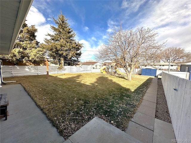 view of yard with a fenced backyard, a storage unit, a playground, and an outbuilding