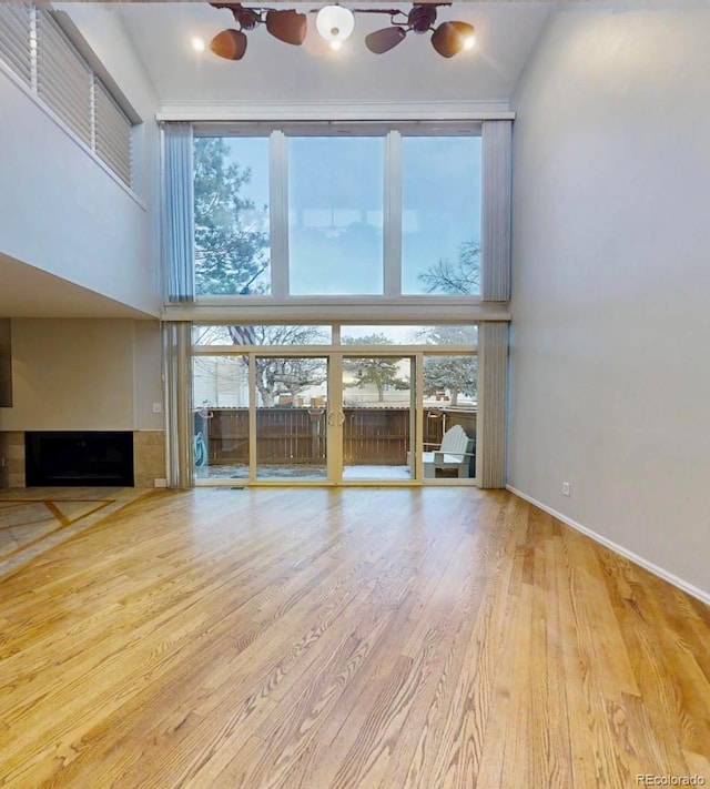 unfurnished living room featuring a towering ceiling, wood finished floors, a fireplace, and baseboards