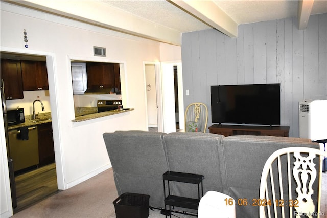 carpeted living room featuring beamed ceiling, a textured ceiling, wooden walls, and sink