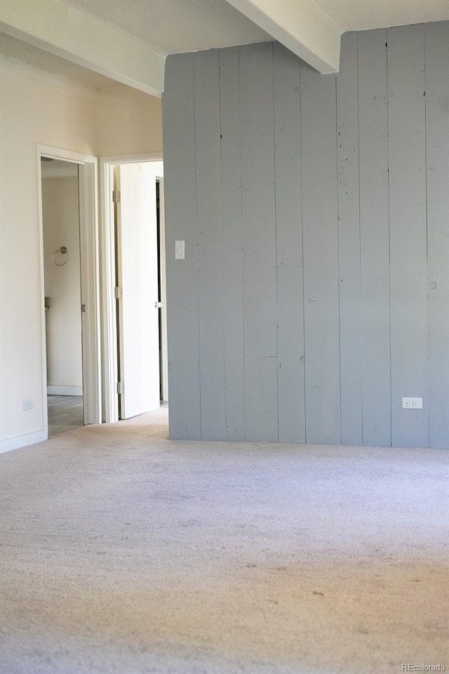 carpeted spare room featuring beam ceiling and wooden walls