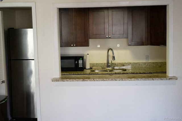 kitchen featuring stainless steel refrigerator, light stone countertops, sink, and dark brown cabinetry