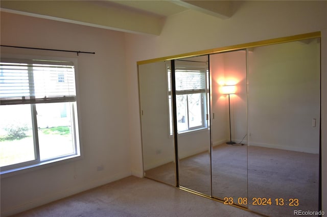 unfurnished bedroom featuring beam ceiling, light colored carpet, and a closet