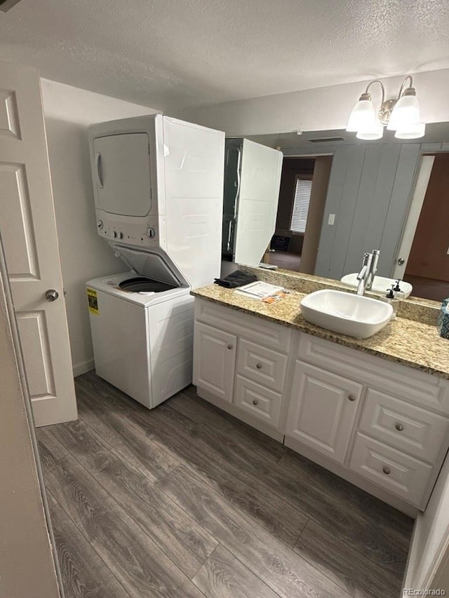 clothes washing area with a textured ceiling, dark hardwood / wood-style flooring, sink, and stacked washer and dryer