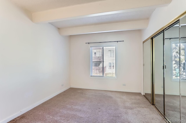 unfurnished bedroom featuring multiple windows, beam ceiling, light colored carpet, and a closet