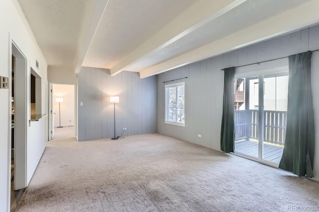 unfurnished room featuring beamed ceiling, light colored carpet, and a textured ceiling