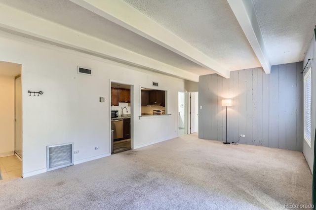 unfurnished living room featuring light colored carpet, a textured ceiling, beam ceiling, and wood walls