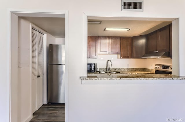 kitchen featuring sink, dark wood-type flooring, appliances with stainless steel finishes, dark brown cabinets, and light stone counters