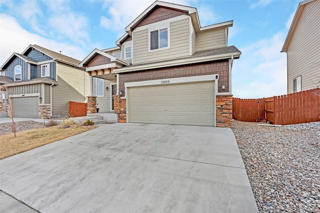 craftsman-style home featuring a garage, stone siding, fence, and driveway