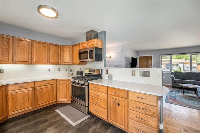 kitchen featuring stainless steel appliances, light countertops, dark wood-type flooring, open floor plan, and a peninsula