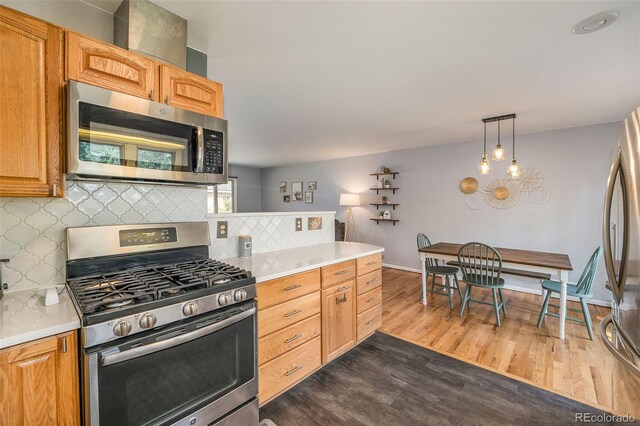 kitchen with dark wood-style floors, hanging light fixtures, stainless steel appliances, light countertops, and backsplash