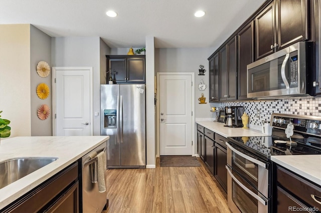 kitchen featuring appliances with stainless steel finishes, dark brown cabinetry, light hardwood / wood-style flooring, and backsplash