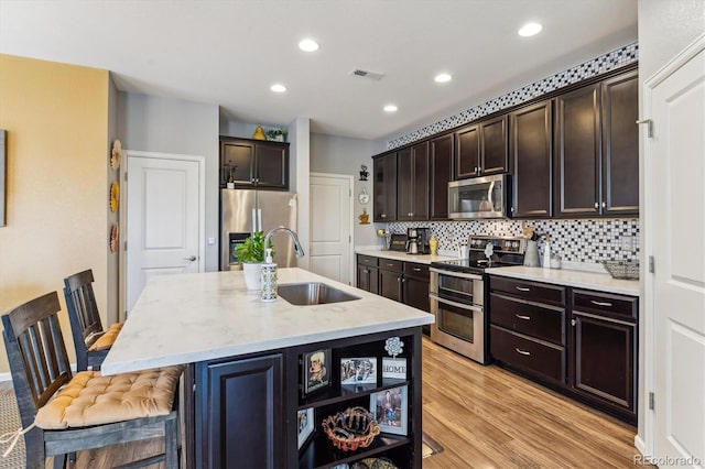 kitchen with tasteful backsplash, a breakfast bar, stainless steel appliances, a kitchen island with sink, and sink