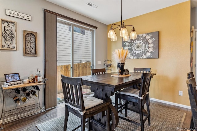 dining area with dark wood-type flooring and an inviting chandelier