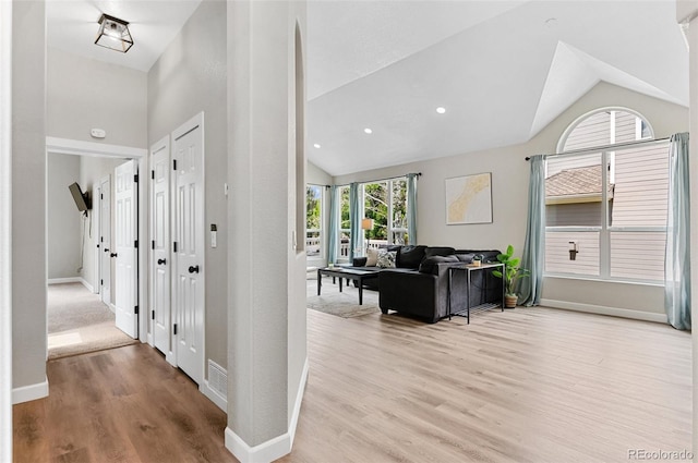 corridor with high vaulted ceiling and light hardwood / wood-style floors