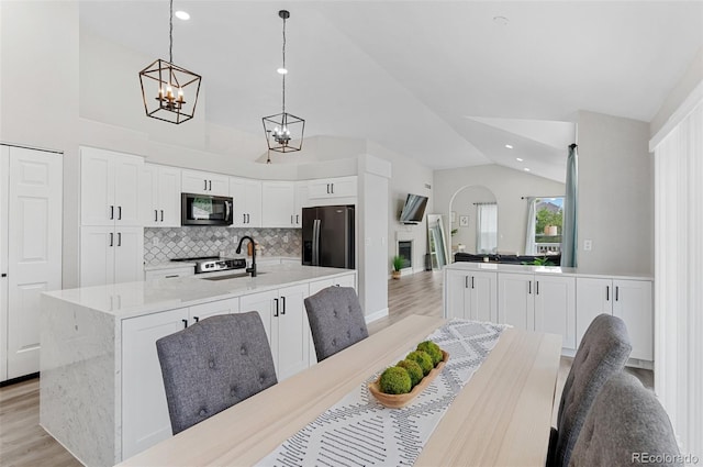 dining space featuring light wood-type flooring, sink, a notable chandelier, and lofted ceiling