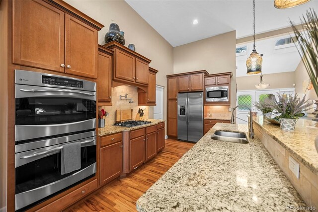 7717 S Grape Ct, Centennial, CO 80122 - kitchen featuring appliances with stainless steel finishes, a sink, brown cabinets, decorative backsplash, and light stone countertops
