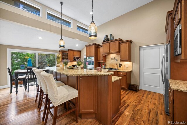 7717 S Grape Ct, Centennial, CO 80122 - kitchen featuring brown cabinetry, stainless steel appliances, wood finished floors, decorative backsplash, and light stone counters