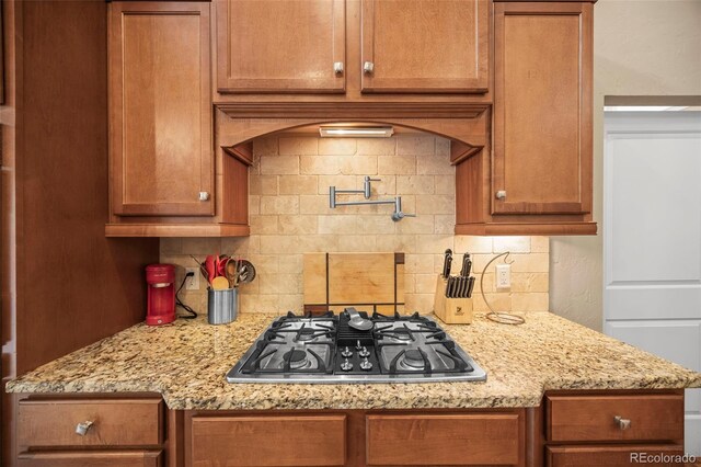 7717 S Grape Ct, Centennial, CO 80122 - kitchen featuring stainless steel gas stovetop, backsplash, brown cabinetry, and light stone counters
