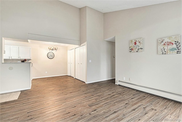 unfurnished living room featuring a baseboard radiator, wood finished floors, high vaulted ceiling, baseboards, and a chandelier