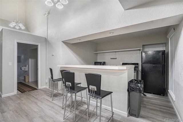 kitchen with freestanding refrigerator, wood finished floors, a chandelier, and a peninsula