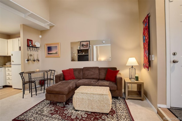 living area featuring a high ceiling, light colored carpet, and baseboards