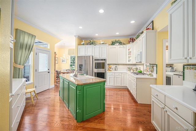 16929 W 63rd Ln, Golden, CO 80403 - kitchen with stainless steel appliances, ornamental molding, an island with sink, white cabinetry, and wood finished floors