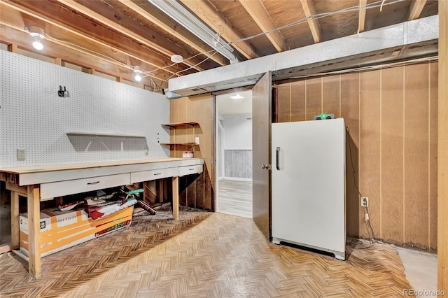 basement featuring light parquet floors, white fridge, and a workshop area