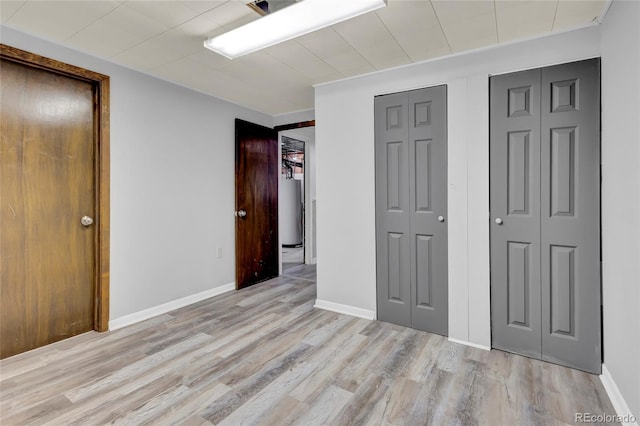 unfurnished bedroom with multiple closets, light hardwood / wood-style flooring, and gas water heater