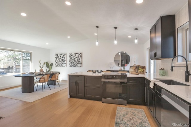 kitchen featuring light wood-style flooring, stainless steel appliances, a peninsula, a sink, and light countertops