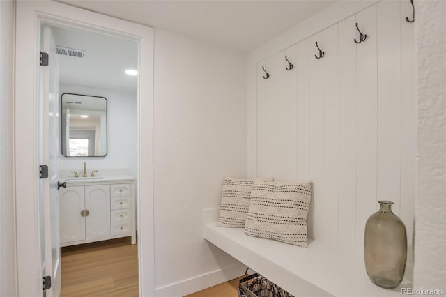 mudroom featuring visible vents, a sink, baseboards, and wood finished floors