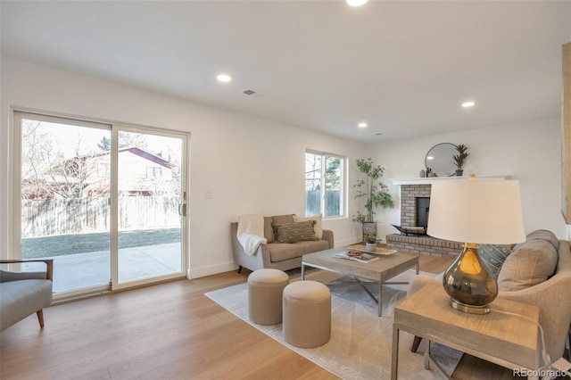 living room with baseboards, visible vents, light wood-style floors, a fireplace, and recessed lighting