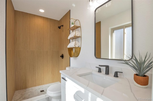 full bathroom with toilet, a tile shower, and vanity