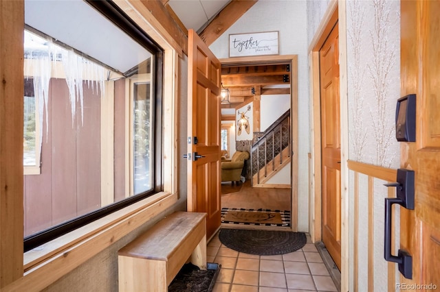 corridor featuring lofted ceiling, light tile patterned flooring, stairs, and a wealth of natural light