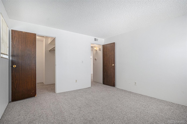 unfurnished bedroom with carpet floors, a spacious closet, a closet, and a textured ceiling