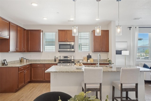 1743 Spring Water Pt, Colorado Springs, CO 80908 - kitchen featuring appliances with stainless steel finishes, a sink, light wood-style flooring, a breakfast bar, and light stone counters