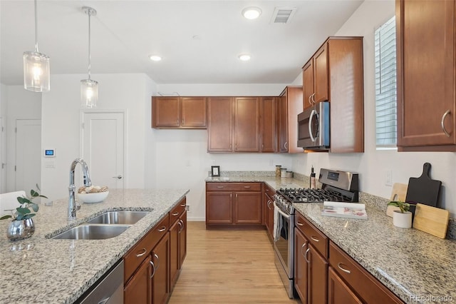 1743 Spring Water Pt, Colorado Springs, CO 80908 - kitchen featuring appliances with stainless steel finishes, a sink, light wood-style floors, hanging light fixtures, and light stone counters