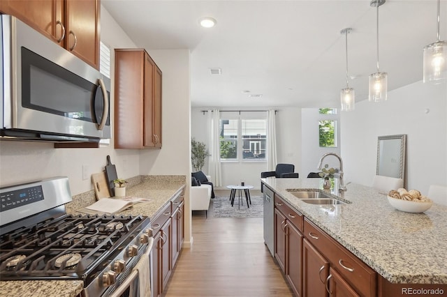 1743 Spring Water Pt, Colorado Springs, CO 80908 - kitchen with stainless steel appliances, a sink, wood finished floors, light stone countertops, and an island with sink