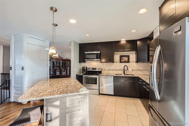 kitchen featuring a center island, sink, light stone countertops, decorative light fixtures, and stainless steel appliances