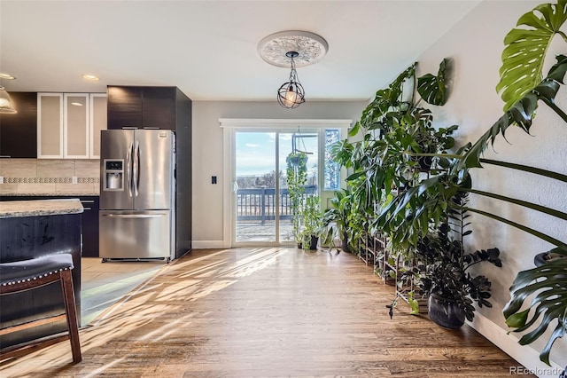 kitchen with light stone countertops, stainless steel fridge with ice dispenser, light hardwood / wood-style flooring, pendant lighting, and decorative backsplash