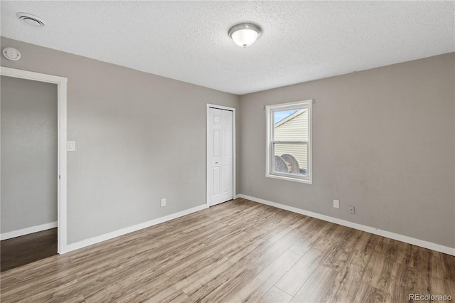 unfurnished bedroom with a textured ceiling, light hardwood / wood-style flooring, and a closet