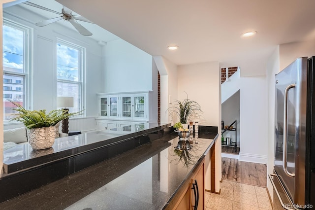 kitchen featuring brown cabinetry, a ceiling fan, baseboards, freestanding refrigerator, and dark stone countertops